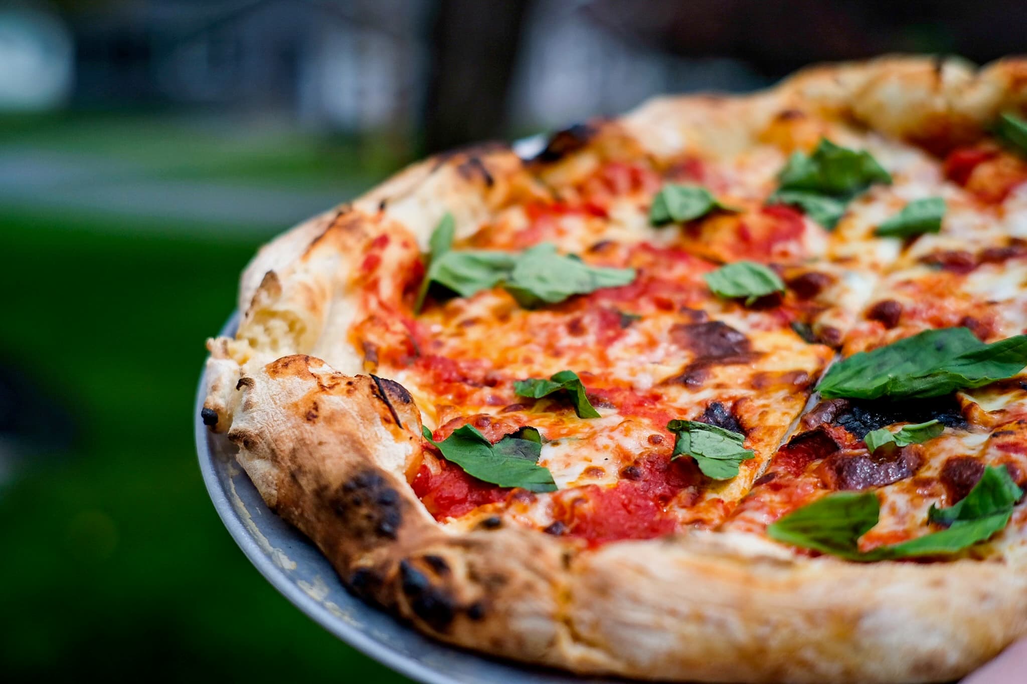 Margherita with basil and char held outside on a metal pan