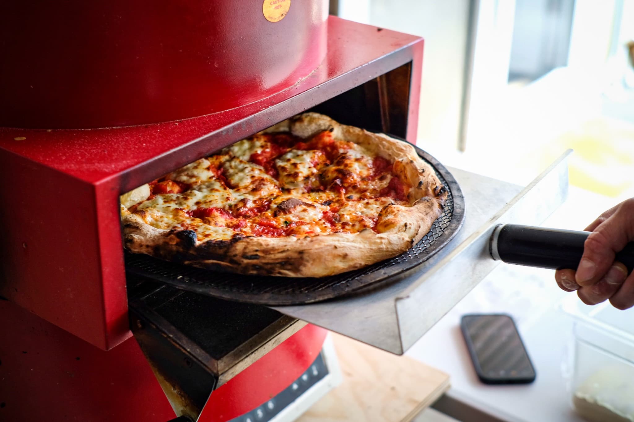 A fresh pizza pulled from the red mobile pizza oven on its peel